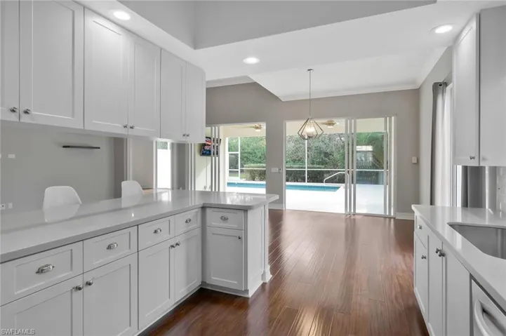 Kitchen featuring light countertops, pendant lighting, stainless steel dishwasher, white cabinets, and dark wood-style flooring