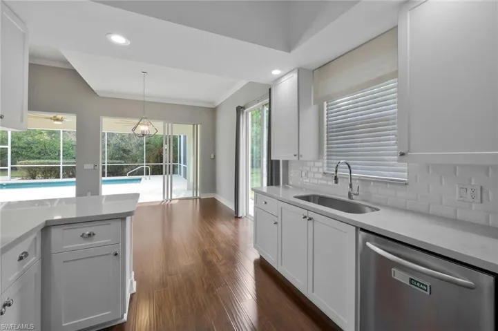 Kitchen featuring light countertops, tasteful backsplash, dark wood-type flooring, a sink, and dishwasher