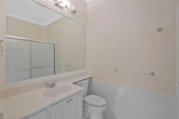 Full bath with crown molding, toilet, vanity, a shower with door, and tile walls