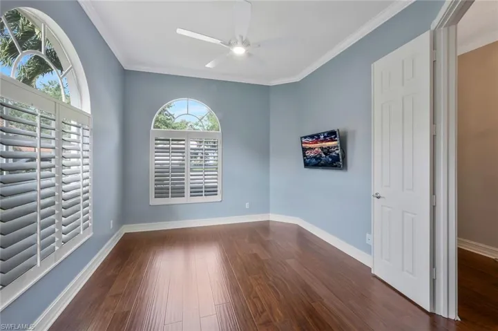 Empty room with crown molding, dark wood-type flooring, baseboards, and ceiling fan