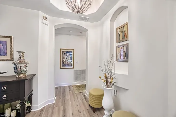 Hall with arched walkways, light wood-style floors, baseboards, and a chandelier