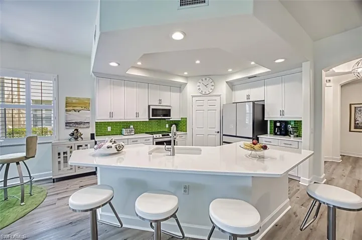 Kitchen with freestanding refrigerator, a sink, light wood-style flooring, a breakfast bar area, and tasteful backsplash