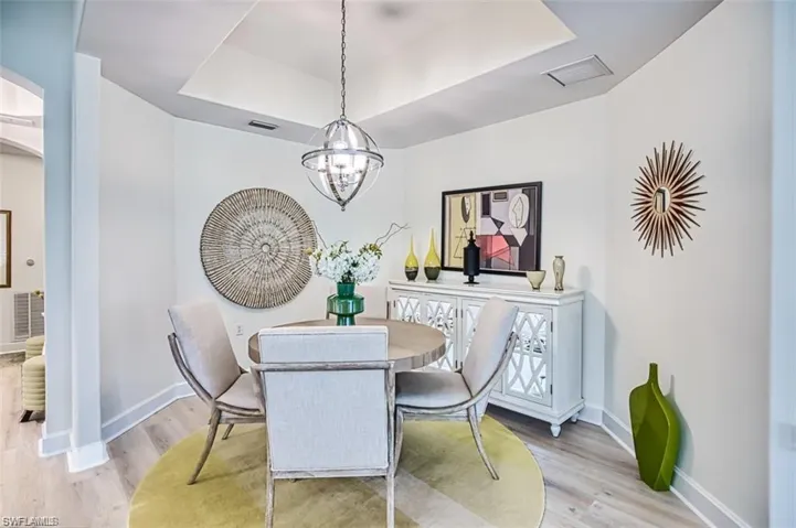 Dining room featuring a tray ceiling, light wood-style floors, arched walkways, and baseboards