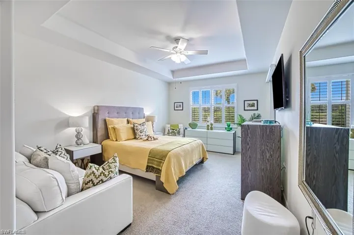 Carpeted bedroom with a tray ceiling and a ceiling fan