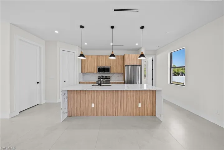 Kitchen with light stone counters, a large island, stainless steel appliances, and pendant lighting