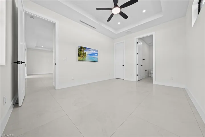 Unfurnished bedroom featuring a tray ceiling, recessed lighting, a ceiling fan, and connected bathroom