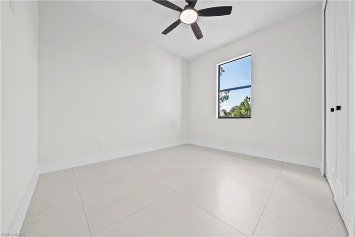 Empty room with a ceiling fan and light tile patterned flooring