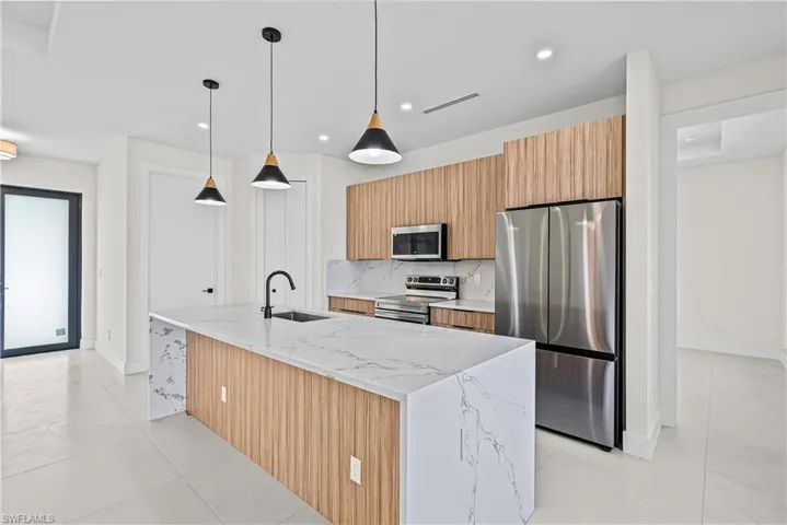 Kitchen with light stone counters, stainless steel appliances, pendant lighting, a kitchen island with sink, and backsplash