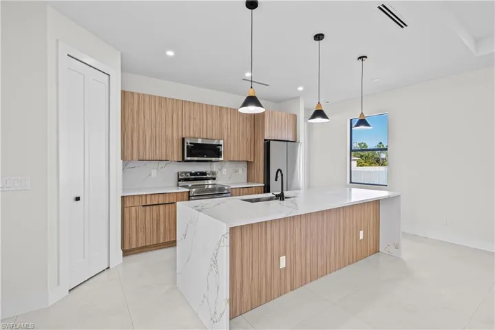 Kitchen with pendant lighting, light stone countertops, stainless steel appliances, modern cabinets, and a kitchen island with sink
