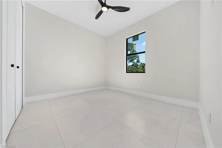 Empty room with ceiling fan, vaulted ceiling, and light tile patterned floors