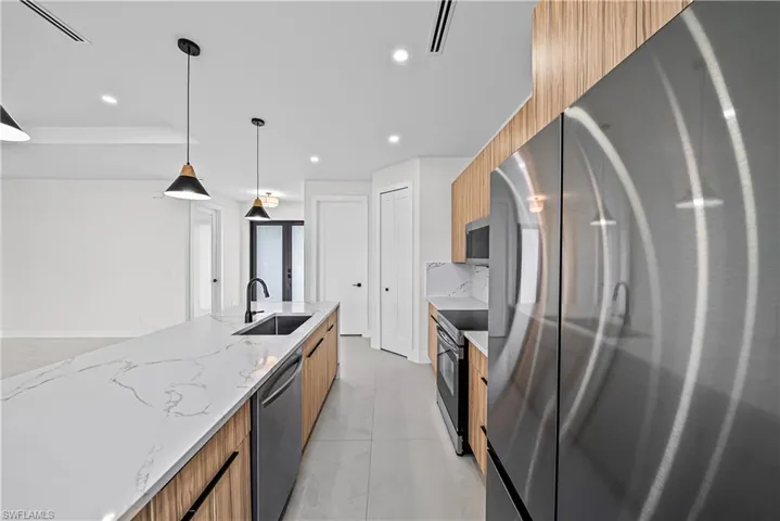Kitchen featuring stainless steel appliances, pendant lighting, light stone countertops, modern cabinets, and wood finish cabinetry