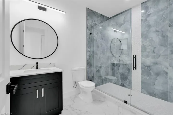 Full bath featuring vanity, a marble finish shower, and marble look tile flooring