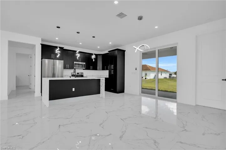 Kitchen featuring dark cabinetry, a center island with sink, stainless steel appliances, open floor plan, and hanging light fixtures