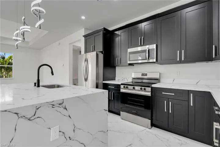 Kitchen with light stone countertops, stainless steel appliances, decorative light fixtures, and dark cabinets