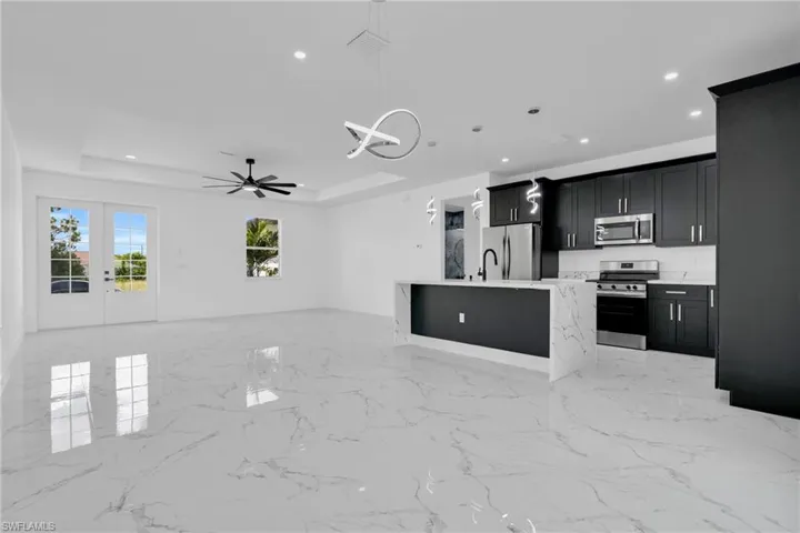Kitchen featuring an island with sink, stainless steel appliances, open floor plan, dark cabinetry, and a ceiling fan