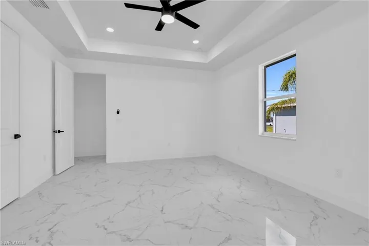 Unfurnished bedroom featuring light marble finish floors, recessed lighting, ceiling fan, and a tray ceiling