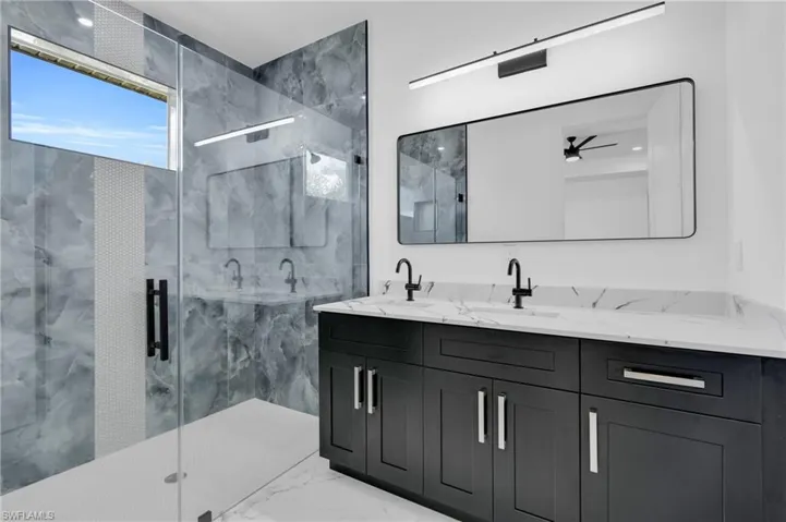Full bathroom with double vanity, a marble finish shower, light marble finish flooring, and ceiling fan