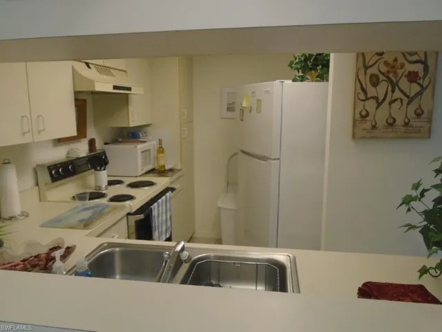 Kitchen with white appliances, sink, white cabinetry, and custom range hood