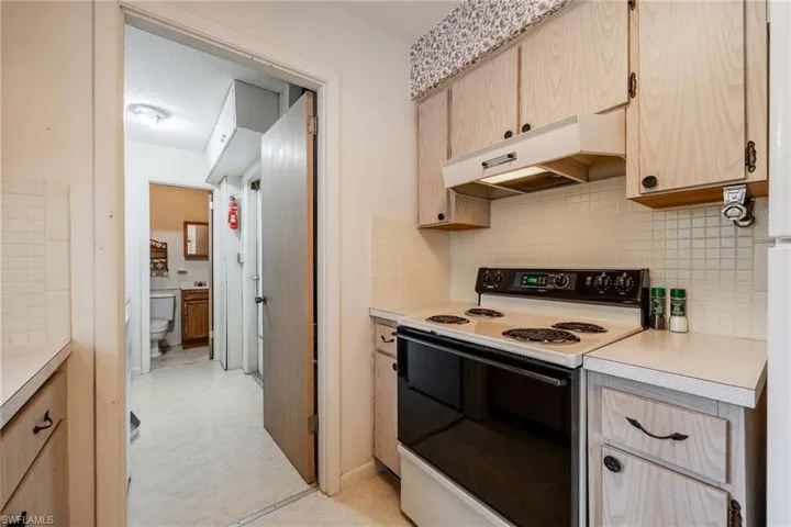 Kitchen featuring electric stove, light brown cabinetry, light countertops, backsplash, and under cabinet range hood