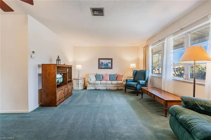Living area featuring carpet flooring, a textured ceiling, visible vents, baseboards, and a ceiling fan