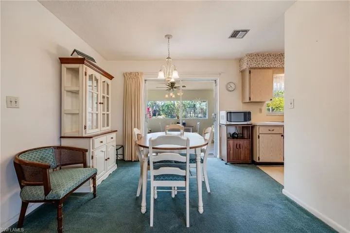 Carpeted dining area with baseboards, visible vents, and a chandelier