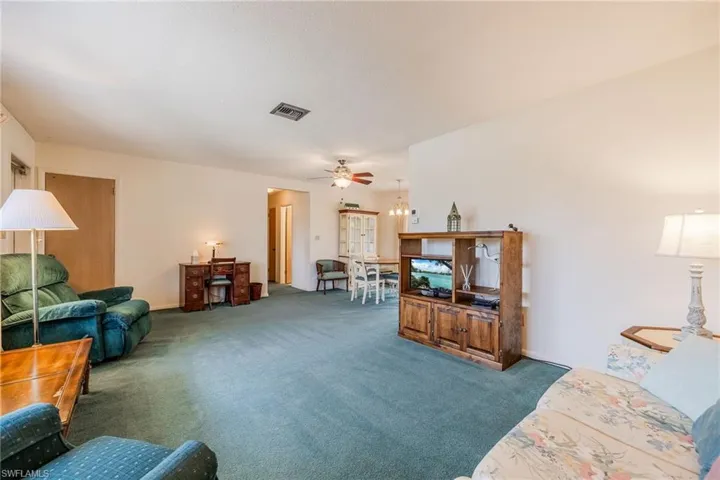 Living room with carpet floors, visible vents, and a ceiling fan