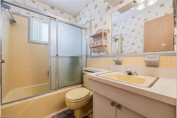 Bathroom with wallpapered walls, vanity, shower / bath combination with glass door, and toilet