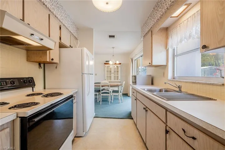 Kitchen with light countertops, light brown cabinetry, range with electric stovetop, and under cabinet range hood
