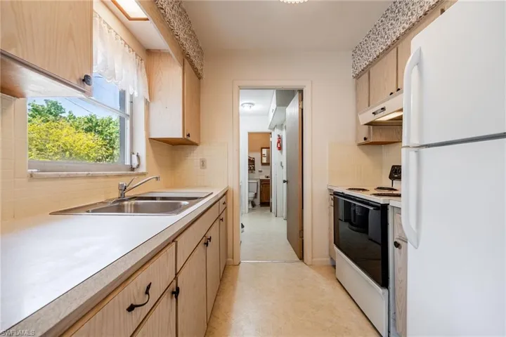 Kitchen with under cabinet range hood, freestanding refrigerator, range with electric cooktop, and light brown cabinetry