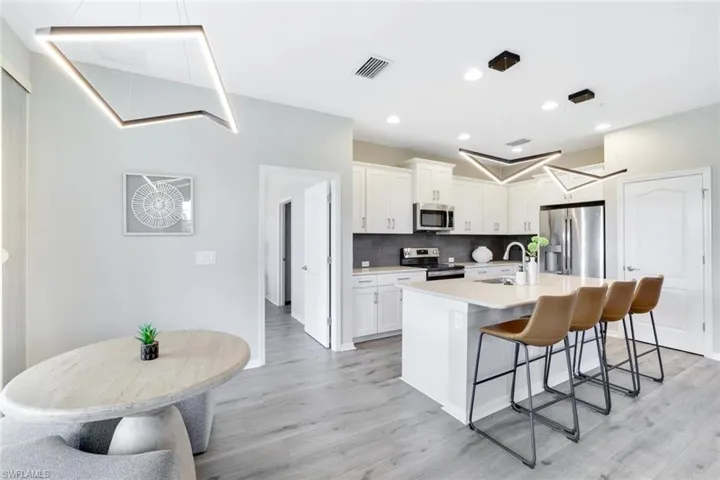 Kitchen featuring backsplash, appliances with stainless steel finishes, white cabinetry, light wood-style flooring, and a kitchen bar