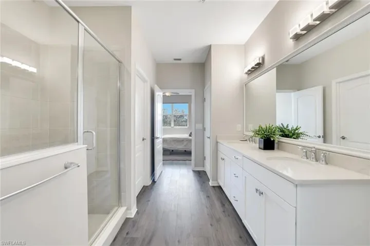 Full bath with connected bathroom, double vanity, a shower stall, and dark wood-style flooring