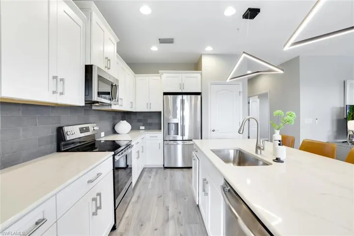 Kitchen with appliances with stainless steel finishes, decorative backsplash, white cabinetry, light stone countertops, and recessed lighting