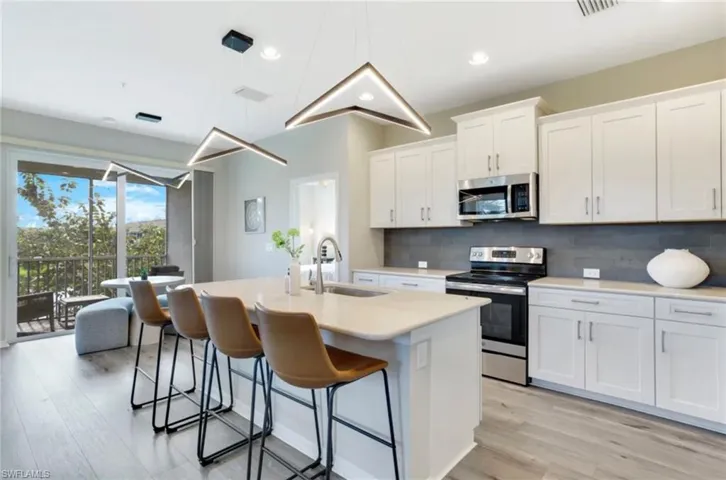 Kitchen featuring appliances with stainless steel finishes, white cabinetry, a kitchen island with sink, hanging light fixtures, and decorative backsplash