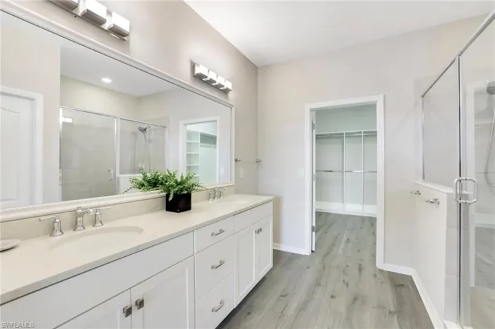 Full bathroom with a walk in closet, a stall shower, double vanity, and light wood-type flooring