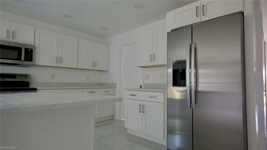 Contemporary kitchen with white shaker-style cabinetry, light-toned countertops, and stainless steel appliances including a side-by-side refrigerator and microwave