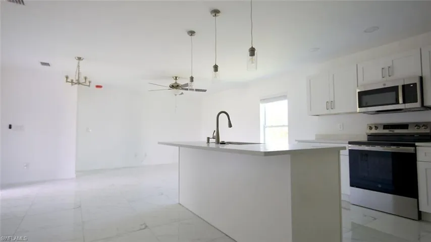 Open-concept kitchen featuring an island with a sink and pendant lighting, stainless steel appliances, white cabinetry, and light countertops