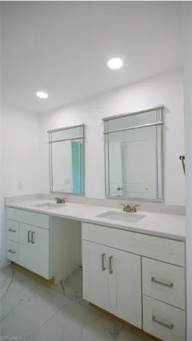 Double vanity featuring white cabinetry with brushed nickel hardware, integrated sinks, and light-toned countertops