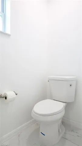 White toilet with a porcelain finish, white baseboards, and marble-look tile flooring