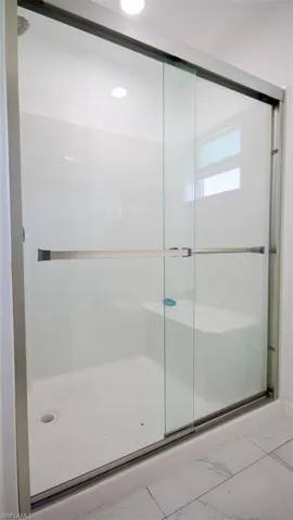 Shower enclosure featuring sliding glass doors with brushed nickel hardware, white subway tile surround, integrated shower bench, and a privacy window