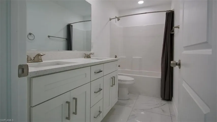 Modern bathroom featuring a dual vanity with a light-toned countertop, brushed nickel fixtures, a full-width mirror, a white bathtub, and large format white tile flooring
