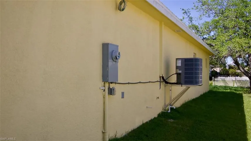 Exterior stucco siding featuring an electrical meter, a wall-mounted AC unit, and a grassy perimeter