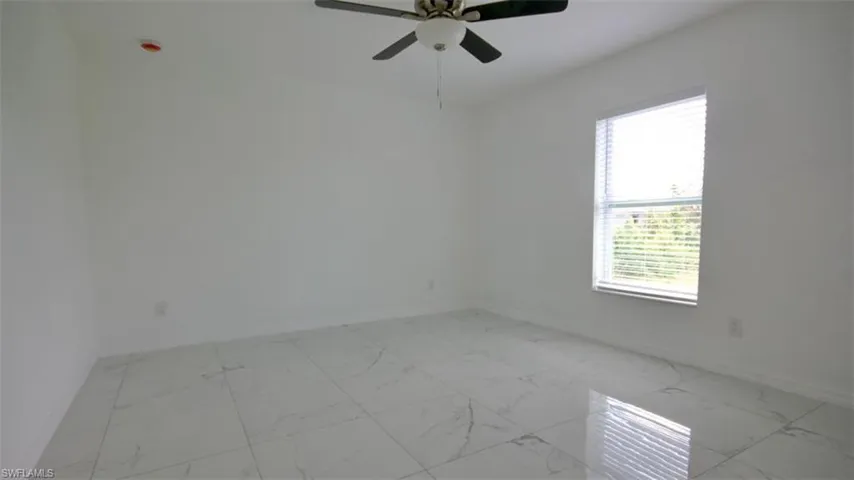 Spacious room featuring white walls, large format tile flooring with subtle veining, a ceiling fan with light fixture, and a window with horizontal blinds