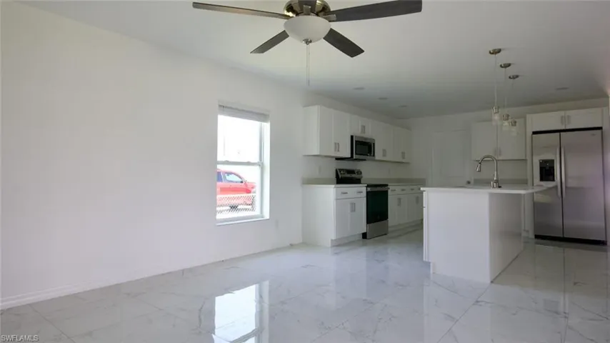 Open concept living space featuring white porcelain tile flooring, a modern kitchen with white cabinetry, stainless steel appliances, and a central island with pendant lighting