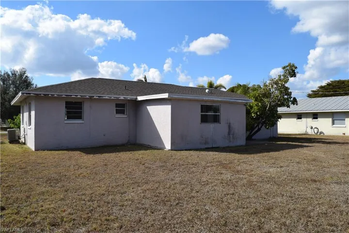 Back of house with stucco siding, a yard, and a shingled roof