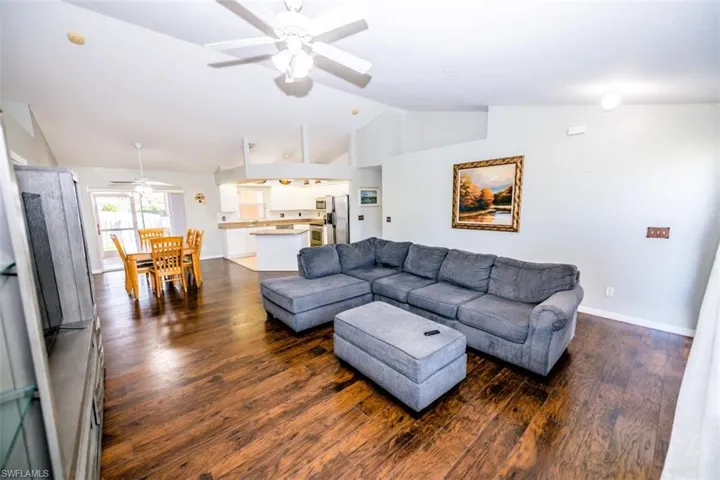 Living room featuring vaulted ceiling, dark wood-style floors, and a ceiling fan