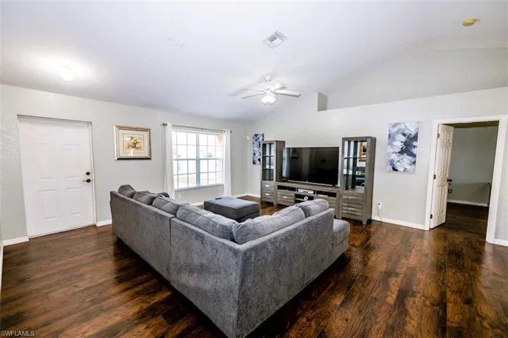Living room with lofted ceiling, ceiling fan, and dark wood finished floors