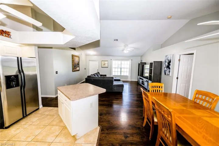 Kitchen with stainless steel refrigerator with ice dispenser, a ceiling fan, vaulted ceiling, a center island, and white cabinets