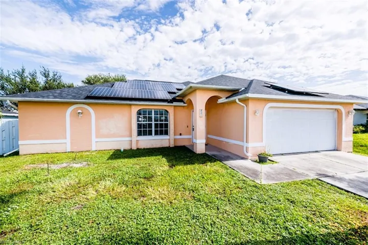 Ranch-style home featuring stucco siding, roof mounted solar panels, a front lawn, and a garage