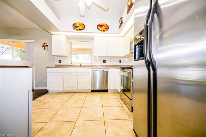 Kitchen with appliances with stainless steel finishes, white cabinets, a ceiling fan, light tile patterned flooring, and decorative backsplash