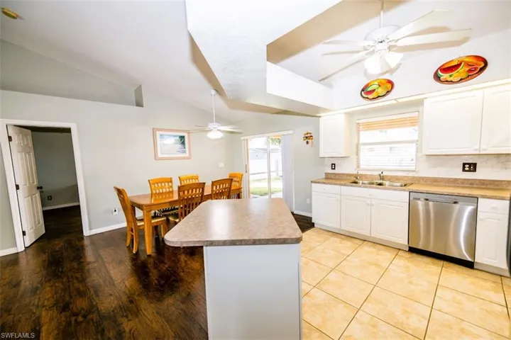 Kitchen with ceiling fan, lofted ceiling, dishwasher, white cabinetry, and a kitchen island
